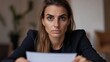 © imagineRbc - A woman is sitting at a table with a piece of paper in front of her. She is wearing a black jacket and has her head tilted