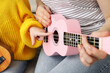 © New Africa - Woman teaching little girl to play ukulele at home, closeup
