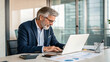 © Kunut - Experienced businessman working on laptop in modern office, focused and engaged