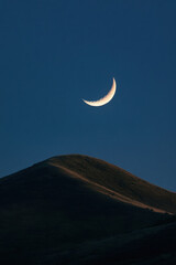 Wall Mural - Serene crescent moon illuminating a peaceful night sky above gently rolling hills.