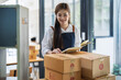 © Jirapong - Young woman engaged in online business working with using notebook, preparing package for shipping and taking notes customer address at box