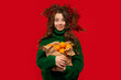 © Vagengeim - Young girl in green sweater holding a paper bag of oranges, wearing a berry wreath, against a red background