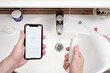 © SKfoto - A man holds a smartphone and an electric toothbrush against bathroom sink.