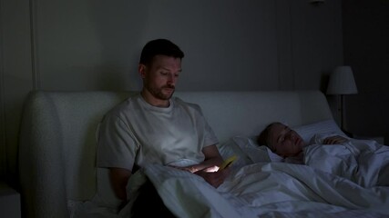 Cheating husband scrolls phone, chats on social networks, messaging in bed at night. Wife sleeps while man betrays absorbed in smartphone, web feed and digital addiction, irregular work schedule