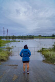 Person in Blue Jacket Observing Flooded Rural Landscape with Submerged Gate and Power Lines