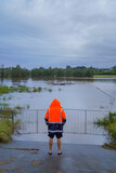 Person in High-Visibility Jacket Observing Flooded Rural Area with Submerged Gate