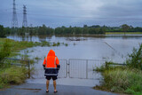 Person in High-Visibility Jacket Observing Flooded Rural Area with Submerged Gate