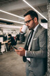 © GutesaMilos - Positive middle aged businessman with beard in suit with cup of coffee using smartphone in office interior, free space. Break of work, video call, app for business, finance and gadget.