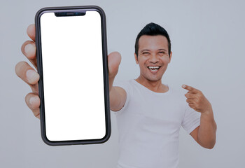 Mobile app advertisement. Handsome excited asian man showing pointing at white empty smartphone screen isolated on white background, Smiling to camera. Check this out, Cellphone display Mock up.