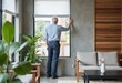 © starush - A man gazes out the window in a modern living room filled with plants