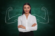 © New Africa - Confident woman with drawing of strong arms behind her on green chalkboard
