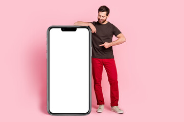 Poster - Full size photo of good mood man dressed brown t-shirt indicating look at smartphone display empty space isolated on pink color background
