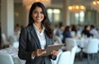 © miss irine - Young Indian woman organizes marketing event. Pro event coordinator holds clipboard. Venue with round tables, people in background. Event management, planning, logistic, organizing, schedule,