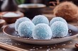 © ANUAR - Delicious Blue Coconut Balls on Plate with Coconut Flakes in Rustic Setting Surrounded by Natural Elements