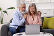 © New Africa - Happy elderly couple looking at laptop on sofa at home