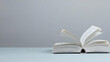 © Imam - Open Book With Flipping Pages On Light Blue Surface Against A Simple Gray Backdrop In A Still Life Setting
