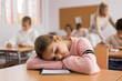 © JackF - Portrait of tired school girl lying and sleeping at desk in classroom during lesson