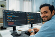 © InfiniteFlow - Smiling smart IT developer working software development looking camera with coding on two pc creating virus firmware application program version on website with coffee cup at modern office. Surmise.