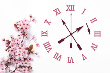 Poster - Clock and blossoming branch with pink flowers on white background, top view. Arrow showing time change one hour ahead in spring. Daylight saving time