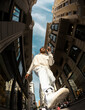 © Jimena Roquero/Stocksy - Fisheye. Full body. Man walking in city street in sunlight from below