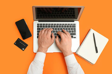 Wall Mural - male hands with laptop, mobile phone and credit card on orange background