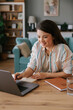 © Mihajlo Ckovric/Stocksy - Woman Smiling While Working on Laptop in Cozy Home Setting
