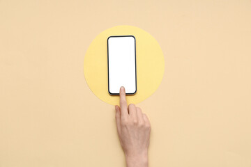 Wall Mural - female hand with mobile phone and blank paper card on beige background