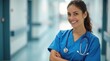 © Kristina - A confident female nurse wearing blue scrubs with a stethoscope around her neck, standing in a bright hospital corridor