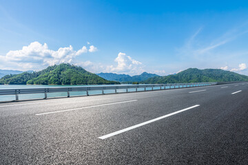 Wall Mural - asphalt road and blue lake with mountain nature landscape under blue sky