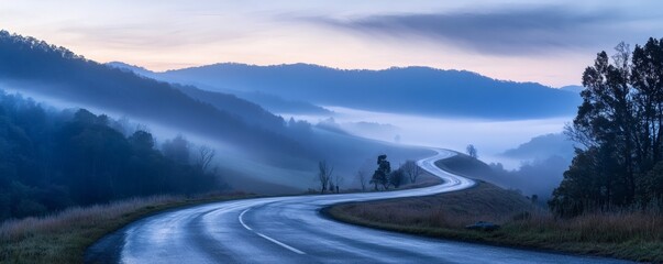 a winding road passes through misty mountains at dawn