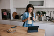 © Mihajlo Ckovric/Stocksy - Smiling Woman Enjoying Coffee While Watching Tablet in Modern Kitchen