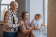 © kuzmichstudio - Grandmother, grandfather and granddaughter playing together at home on the window portrait