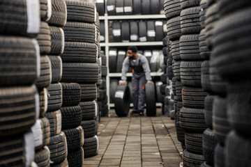 Fototapete - Selective focus on piles of tires with interracial auto mechanic worker rolling tires in a blurry background.