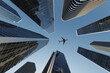 © Bernt Moss/Stocksy - Jet flying in a blue sky  above tall skyscarpers in a city