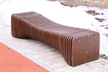 Aufkleber - A simple wooden bench placed on the edge of a sidewalk, suitable for urban scenes or public spaces.