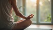 © natakot - A serene figure sits cross-legged on a yoga mat, bathed in the warm glow of sunlight streaming through large windows. The peaceful atmosphere is enhanced by the gentle touch of nature visible outside