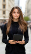 © AMIRIL - Confident young professional woman in business attire holding a tablet in urban setting