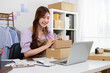 © jojo - A young woman places boxes on her desk to pack her goods.
