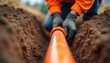© miss irine - Underground pipes installation. Orange pipeline installation by worker in trench. Man connects plastic plumbing pipes. Technician assembles main water system. Repairing main sewerage. Close-up worker