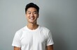 © miss irine - Handsome Asian man smiles, gazes confidently. Man expresses joy, cheerfulness in a studio setting. He has fresh face skin. Man posing in white T-shirt against neutral background.
