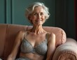 © miss irine - Elegant senior woman poses in grey lace lingerie on a sofa. Beautiful mature lady with wavy bob hairstyle smiles. Aged beauty concept. Intimate portrait of sensual older model indoors.
