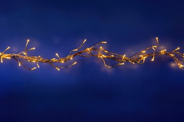Leinwandbilder - Warm golden Christmas garland lights softly glowing, creating a dreamy bokeh effect over a deep blue background