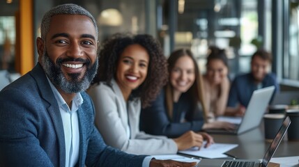 Poster - Smiling group of diverse businesspeople going over paperwork together and working on a laptop at a table in an office