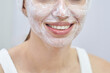 © elenavolf - Female caucasian young adult enjoying skincare routine with face mask at home smiling.