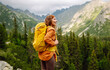 © maxbelchenko - An active female traveler with a bright hiking backpack enjoys the mountain view from the cliff. Young woman feels freedom on a hike. Adventure concept.