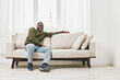 © SHOTPRIME STUDIO - Happy Black man in cozy sweater on beige couch, showcasing comfort and relaxation in a bright, modern living room environment