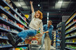 © Zamrznuti tonovi - Happy couple having fun while grocery shopping in supermarket, woman sitting in shopping cart
