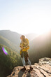 © maxbelchenko - Happy female traveler with colorful backpack enjoying mountain view. Young woman feels freedom standing on cliff. Adventure concept, freedom. Wanderlust.
