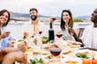 © Xavier Lorenzo - Happy group of multiracial young friends having dinner at rooftop summer party. Multiracial people laughing and having fun while drinking and eating sitting on table during celebration