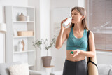 Sporty young woman drinking tasty yogurt at home